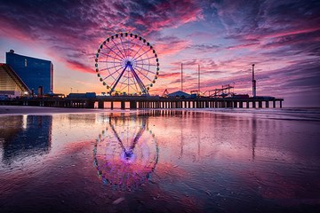 Steel Pier and The Wheel ferris wheel are reflected in the shoreline during sunrise in Atlantic City.